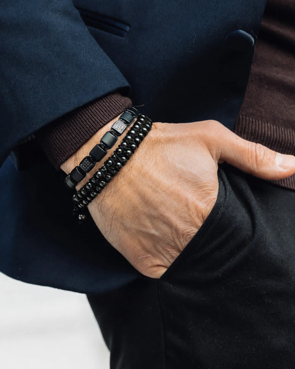 Black bracelet stack on wrist featuring braided cord and rectangular bead segments
