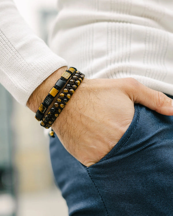 Wrist wearing a black multi-strand bracelet with gold tiger-eye detailing and metal beads