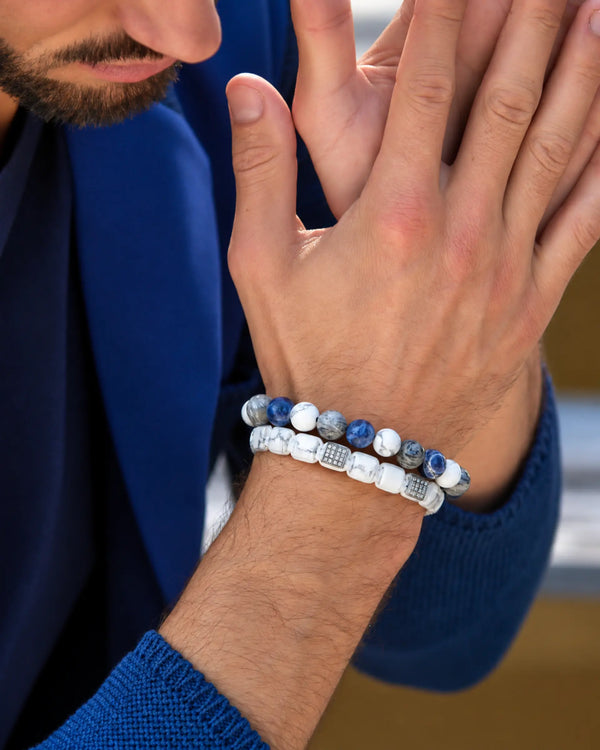 Two beaded bracelets on wrist: white/blue Howlite and dark bracelet with center bar