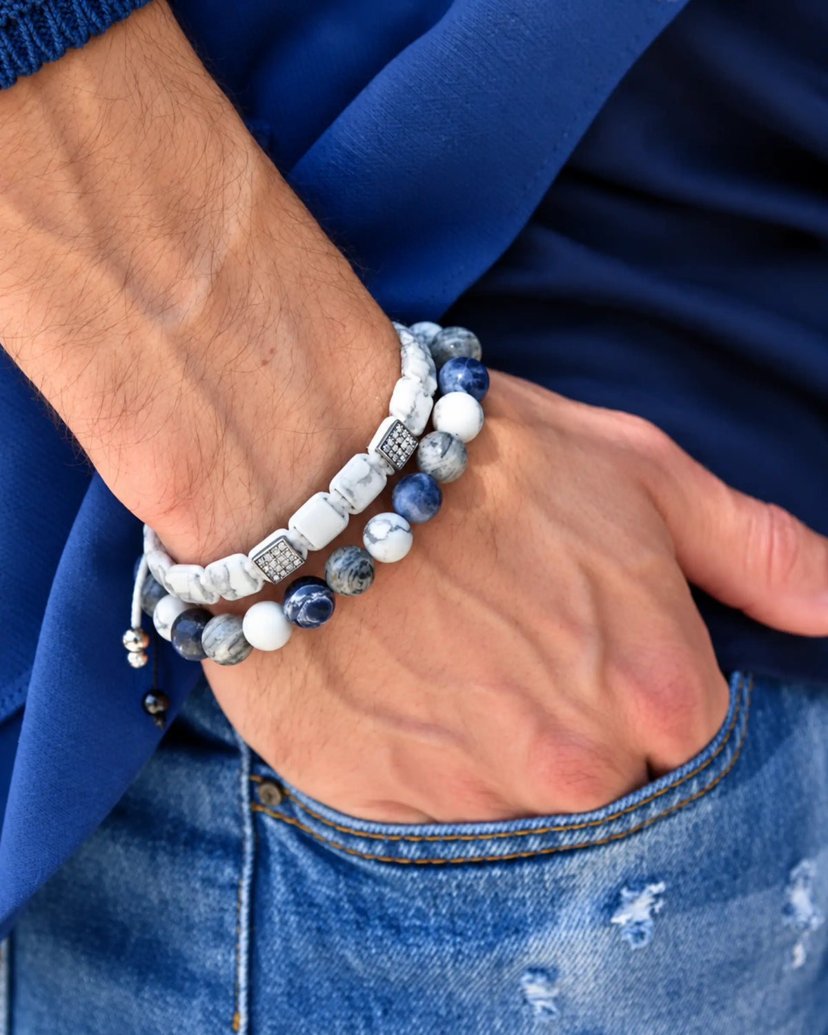 Stacked beaded bracelets on wrist with white, blue, gray beads and dark braided band