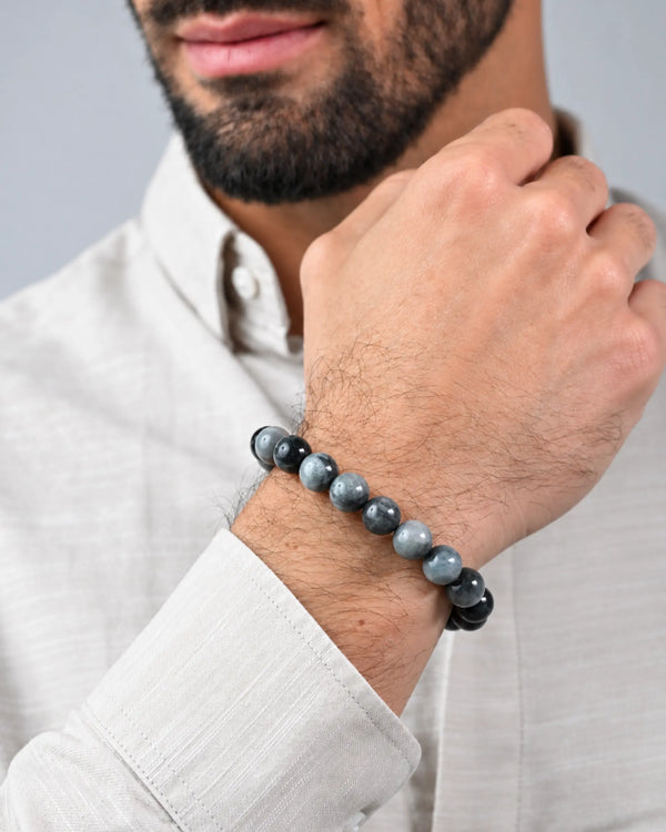 Beaded bracelet on wrist with gray stones and black braided cord, metal center tag
