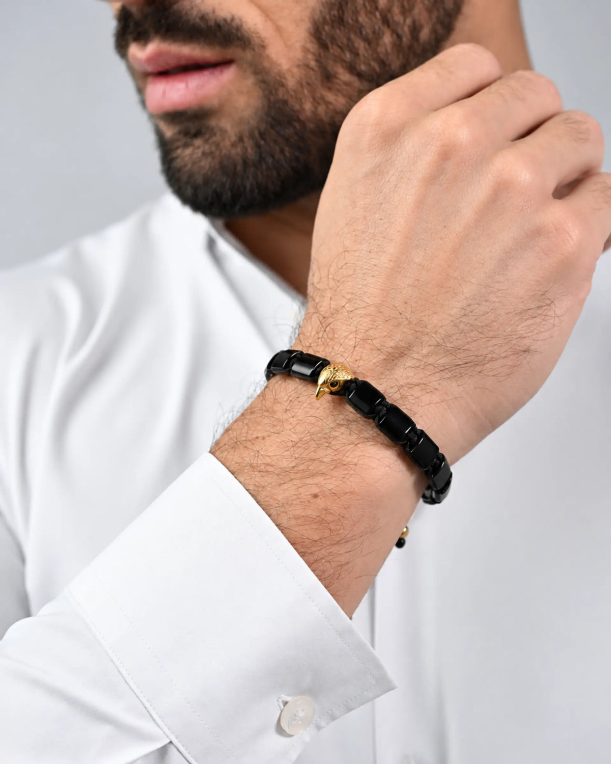 Black and gold falcon bracelet worn on wrist with white shirt cuff