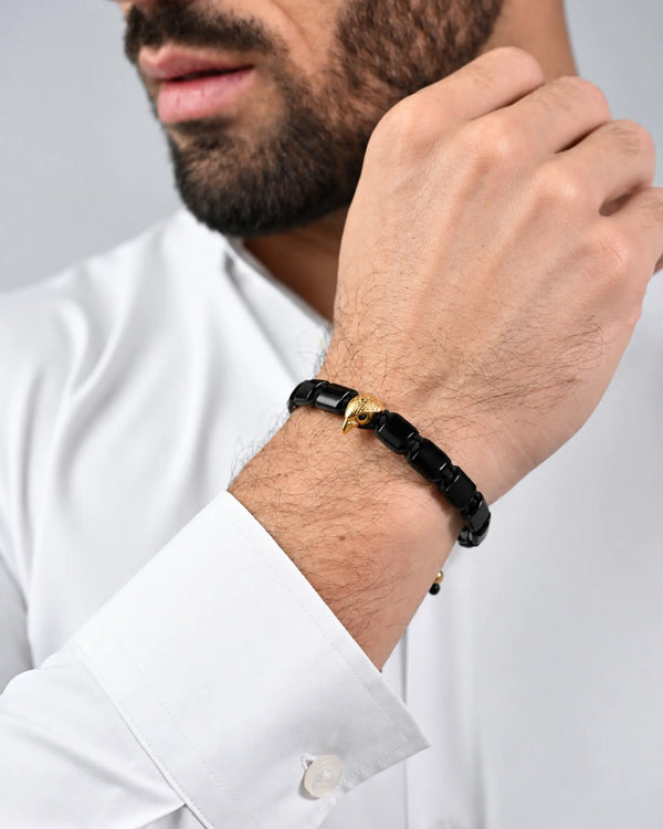 Black and gold falcon bracelet worn on wrist with white shirt cuff