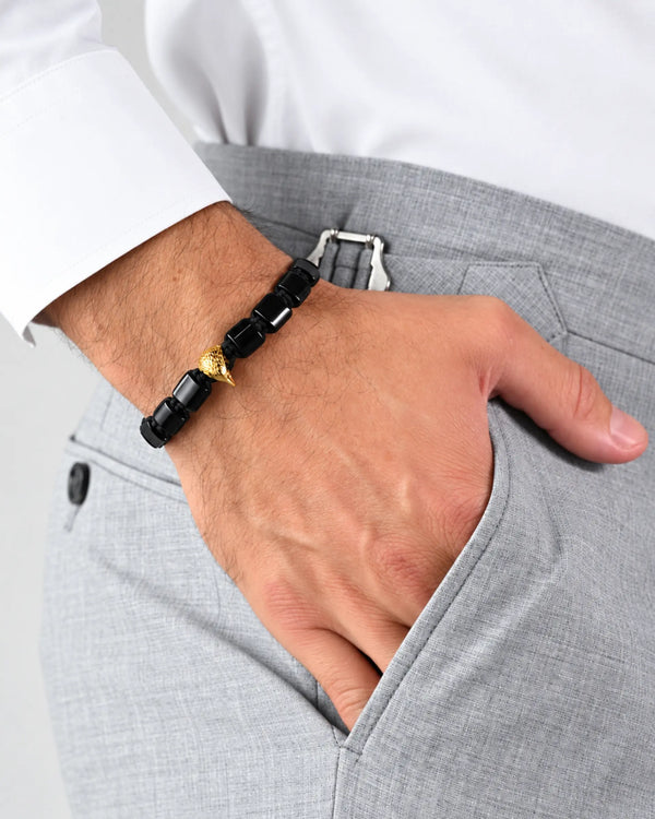 Black and gold falcon bracelet worn on wrist with grey trousers