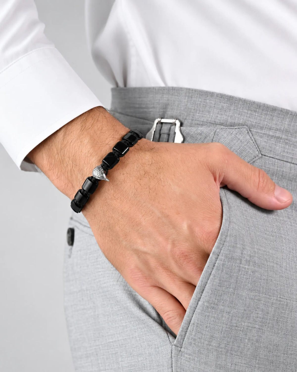 Black beaded bracelet with silver centerpiece worn on hand with gray pants