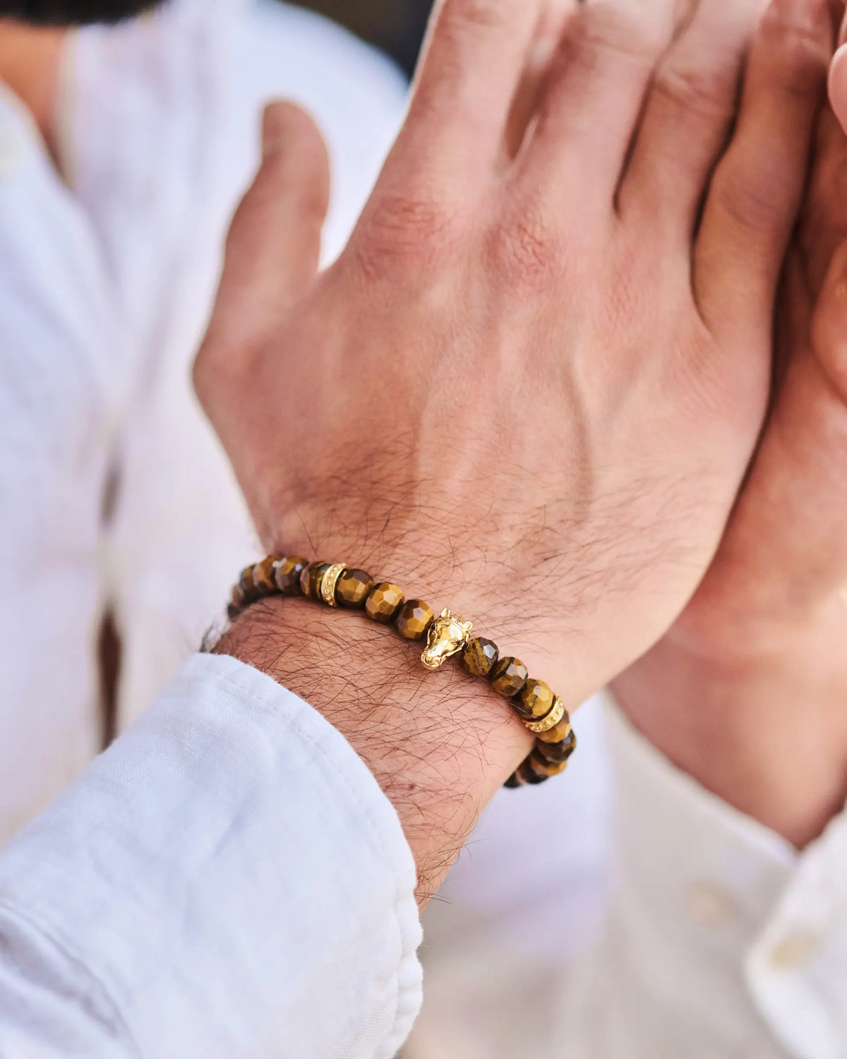 Tiger eye bead bracelet with gold-tone accents worn on wrist with black cord.