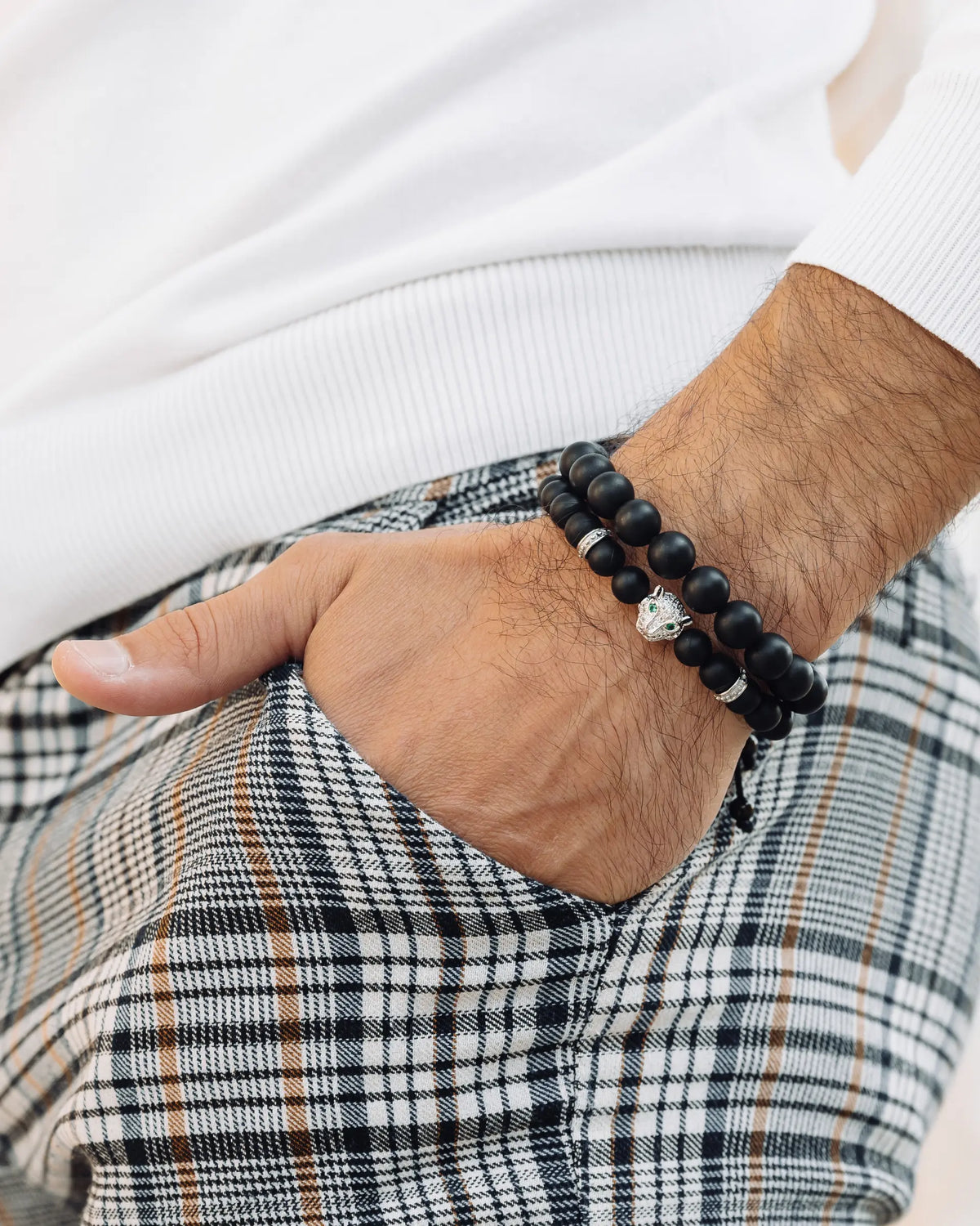 Two black beaded bracelets with silver charm on a man’s wrist