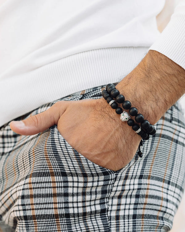 Two black beaded bracelets with silver charm on a man’s wrist